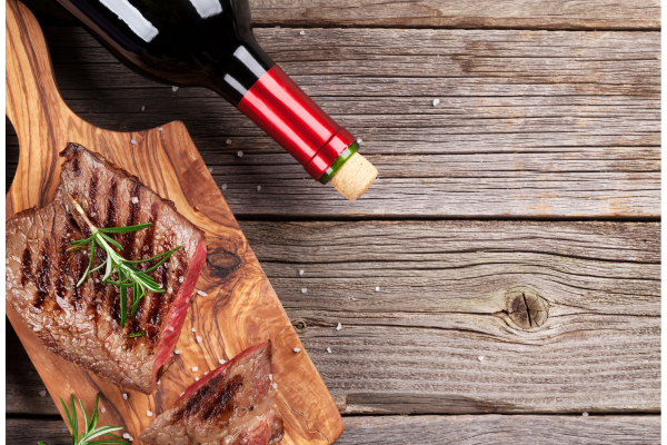 red wine bottle on its side next to a board with sliced steak